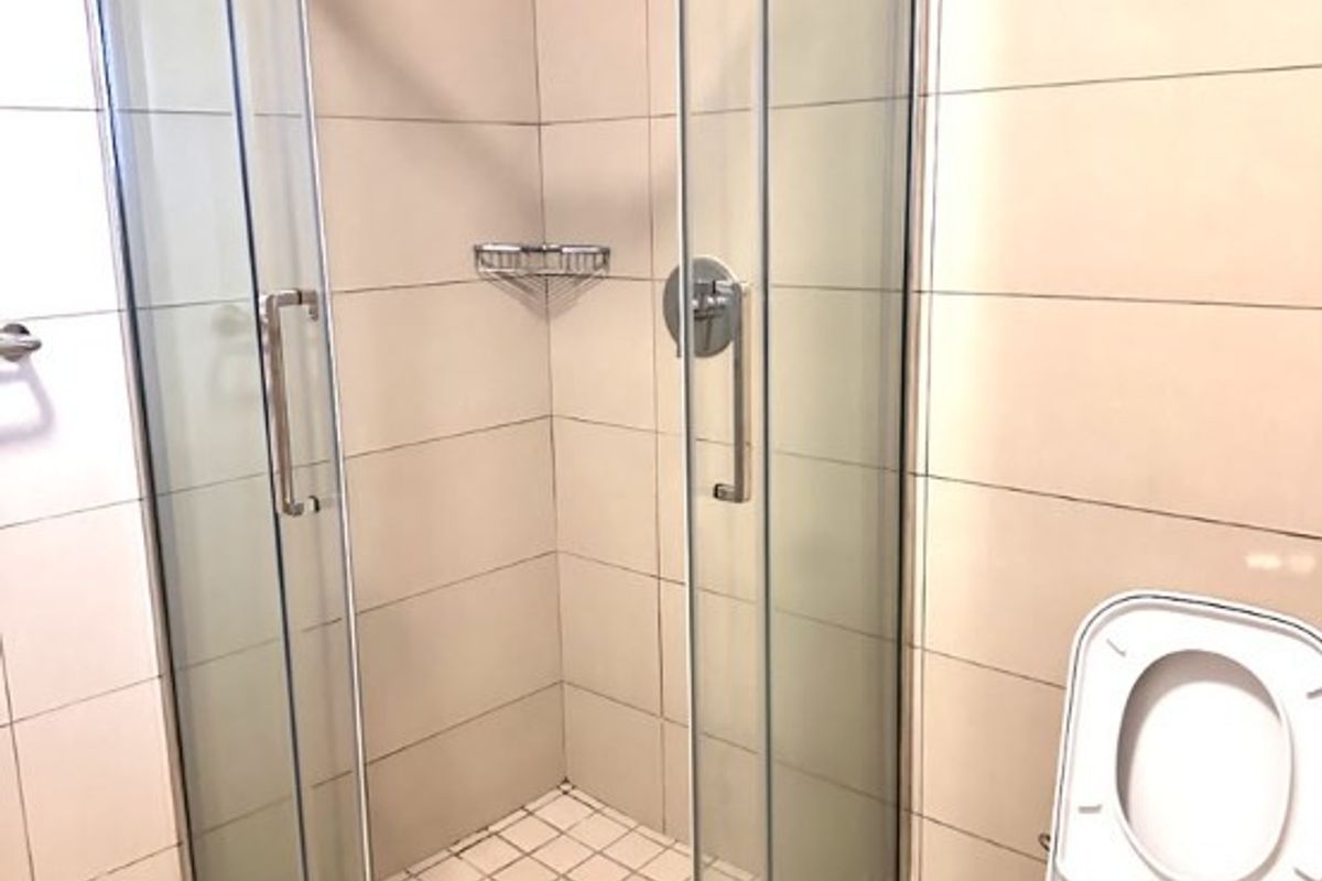 A clean, modern bathroom featuring a glass corner shower enclosure, tiled walls and flooring, and a standard toilet.