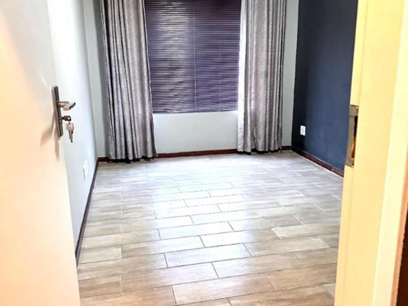 A clean, empty bedroom featuring modern tiled flooring, a dark accent wall, and window treatments.