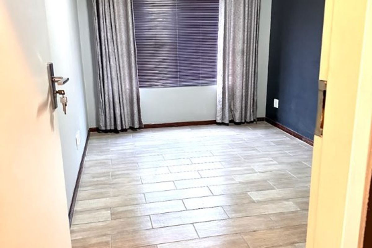 A clean, empty bedroom featuring modern tiled flooring, a dark accent wall, and window treatments.