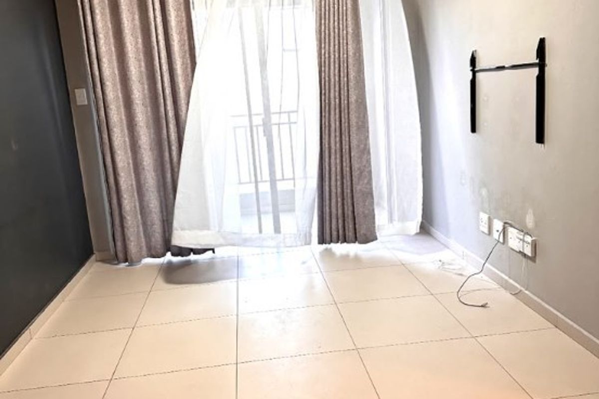 An empty living room featuring tiled flooring, a wall-mounted television bracket, and a sliding glass door leading to a balcony.