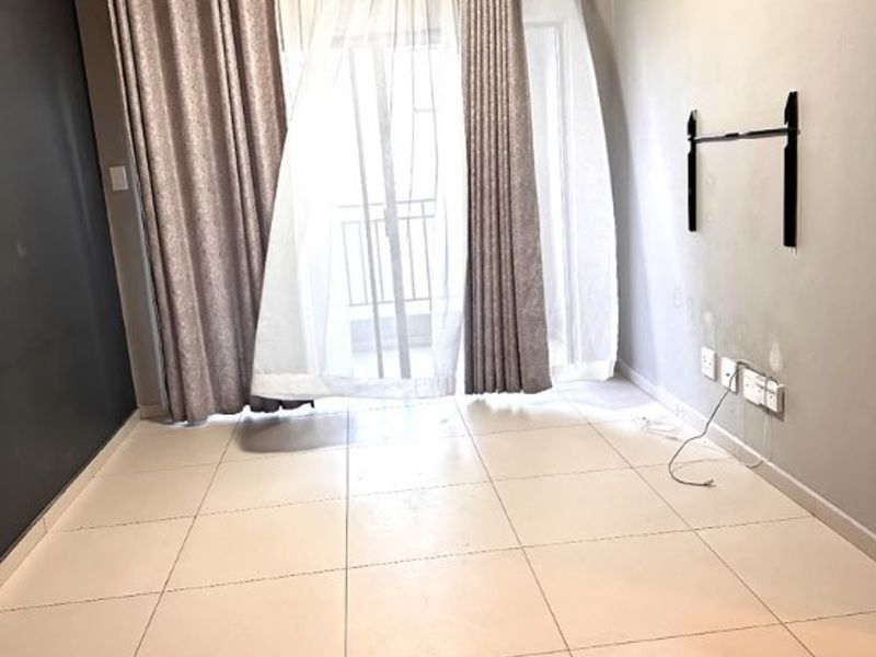 An empty living room featuring tiled flooring, a wall-mounted television bracket, and a sliding glass door leading to a balcony.