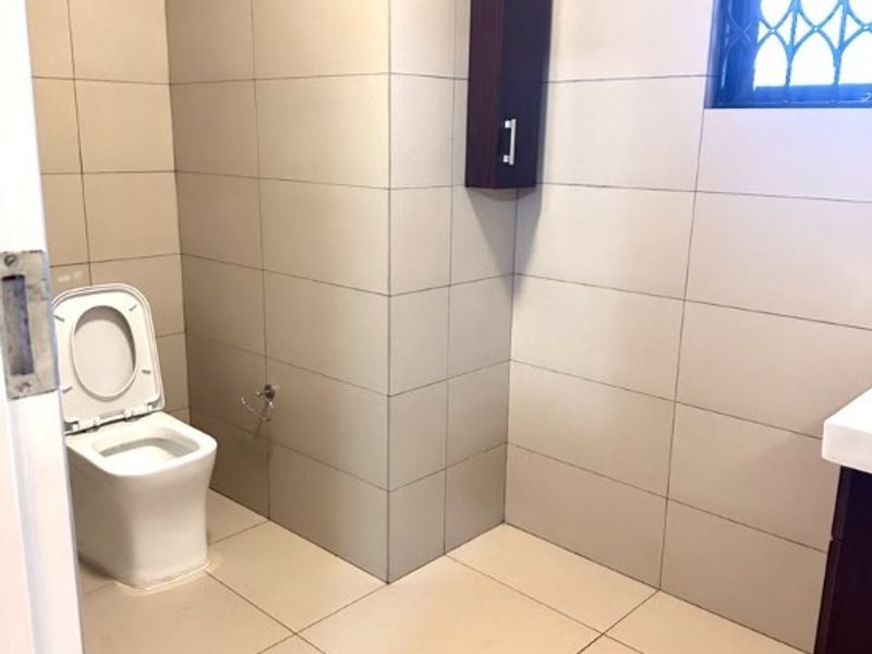 A clean, tiled bathroom featuring a modern toilet, vanity cabinet, and a window with a security gate.