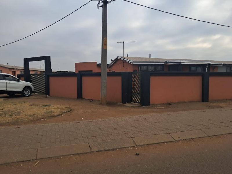 Front view of a residential property featuring a perimeter wall, metal gate, and paved driveway access.