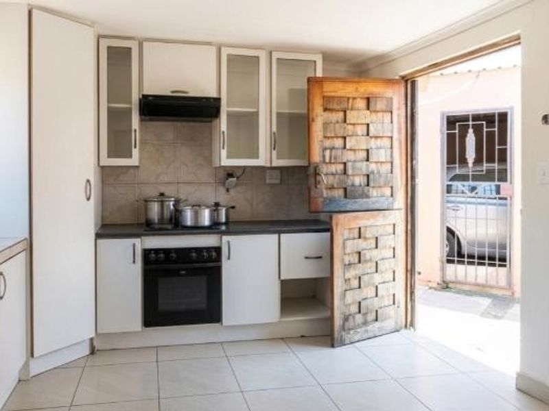 Compact kitchen featuring white built-in cabinetry, an electric oven with extractor fan, tiled flooring, and a unique wooden stable door leading to the exterior.