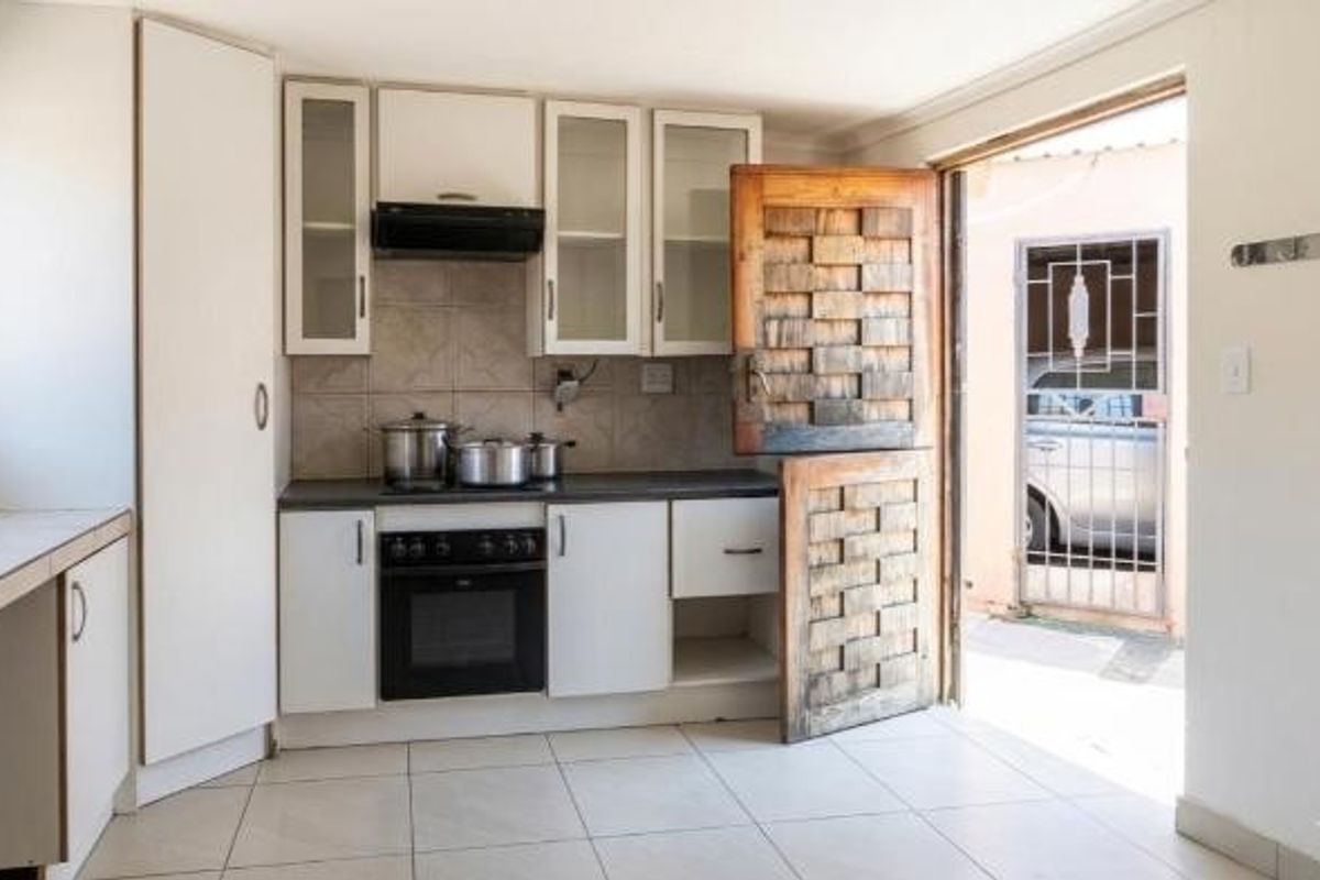 Compact kitchen featuring white built-in cabinetry, an electric oven with extractor fan, tiled flooring, and a unique wooden stable door leading to the exterior.
