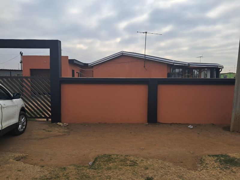 Front exterior view of a residential property featuring a perimeter wall, metal gate, and pitched roof structure.