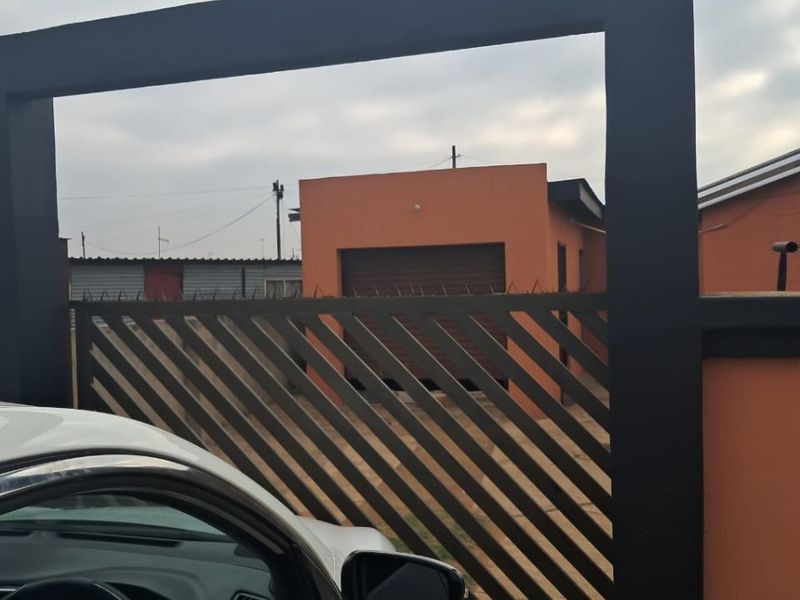 Front view of the property featuring a modern sliding gate, perimeter wall with security razor wire, and a single garage.