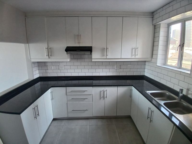 A modern, clean kitchen featuring white cabinetry, contrasting black granite countertops, subway tile backsplash, and a stainless steel double sink.