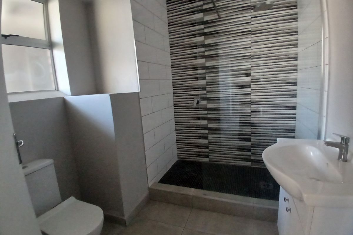 A modern bathroom featuring a walk-in shower with decorative tiled accent wall, a vanity basin, and a toilet.