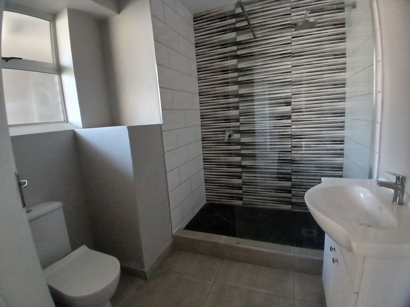 A modern bathroom featuring a walk-in shower with decorative tiled accent wall, a vanity basin, and a toilet.