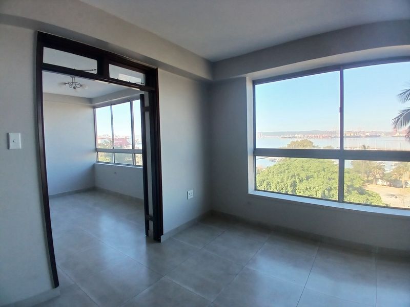 Bright and spacious living area featuring large windows with scenic views, neutral tiled flooring, and an open-plan layout connecting to an adjacent sunroom.