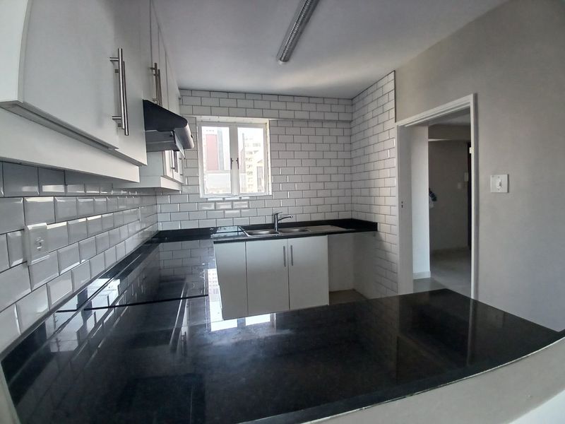 A clean, modern kitchen featuring white subway tile backsplash, dark granite countertops, and ample built-in cabinetry with an integrated extractor fan.