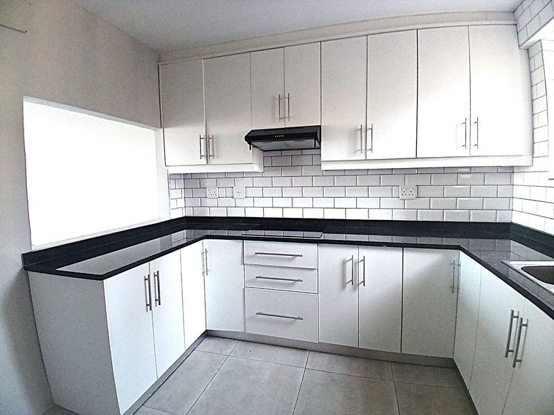 A clean, modern kitchen featuring white cabinetry, contrasting black stone countertops, subway tile backsplash, and integrated extractor fan.