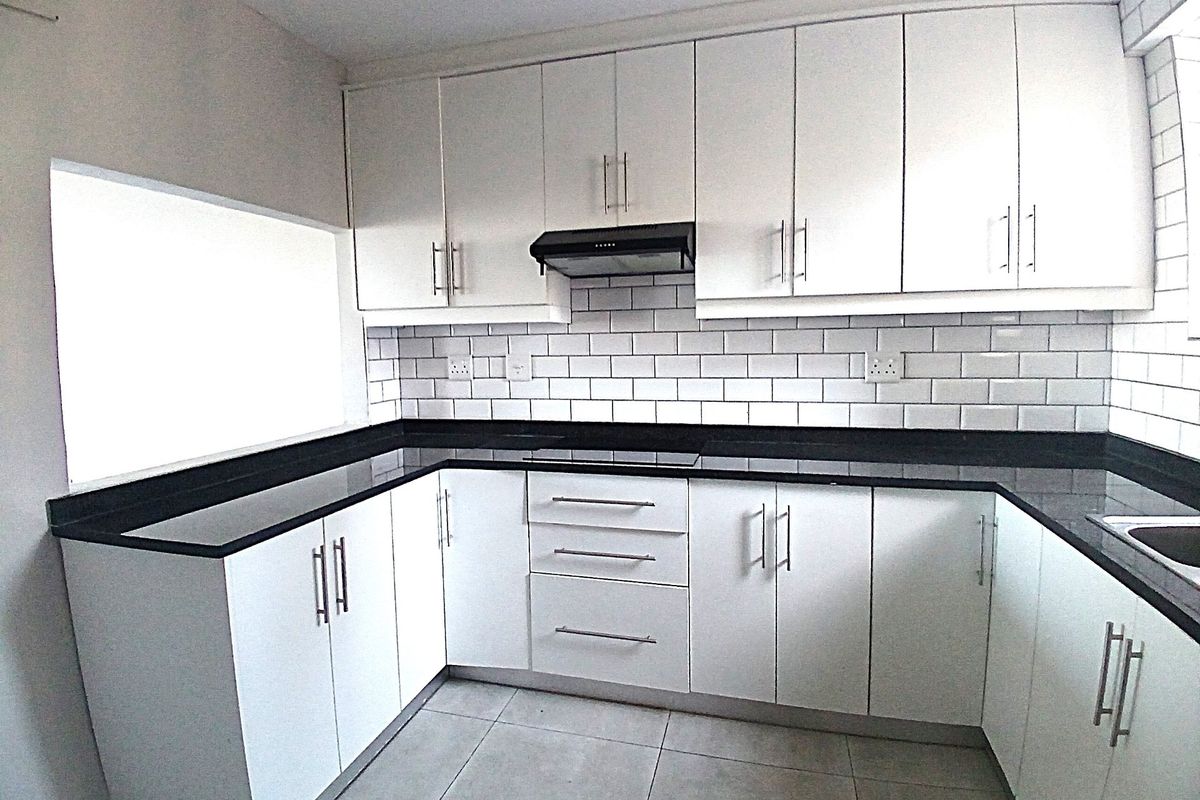 A clean, modern kitchen featuring white cabinetry, contrasting black stone countertops, subway tile backsplash, and integrated extractor fan.