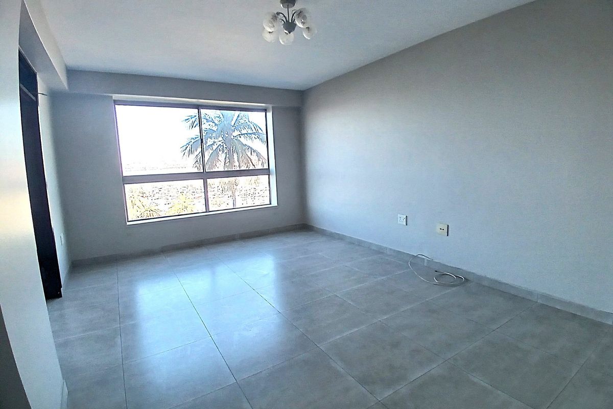 A bright, empty bedroom featuring neutral tiled flooring, a large window providing natural light, and a modern ceiling light fixture.
