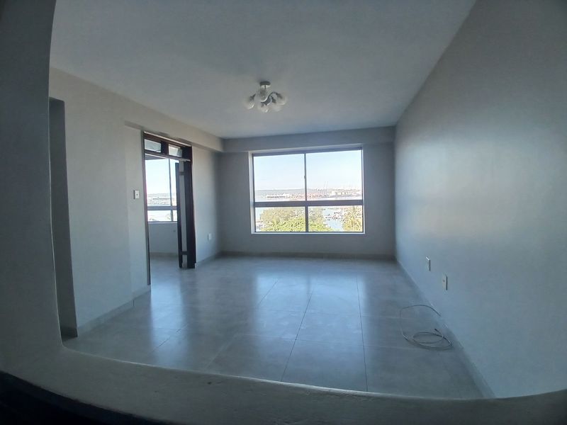 An empty, well-lit living area featuring neutral tiled flooring, a large window with scenic views, and access to an adjoining space.