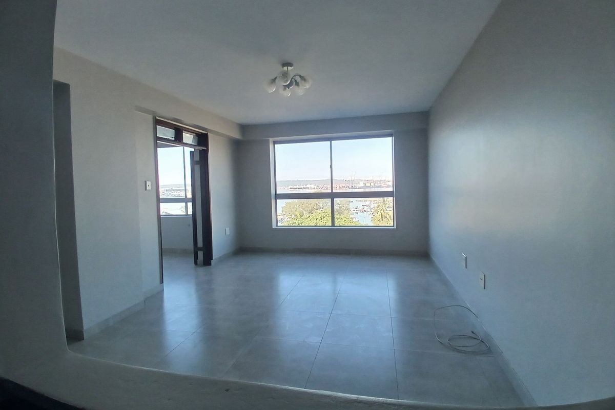 An empty, well-lit living area featuring neutral tiled flooring, a large window with scenic views, and access to an adjoining space.