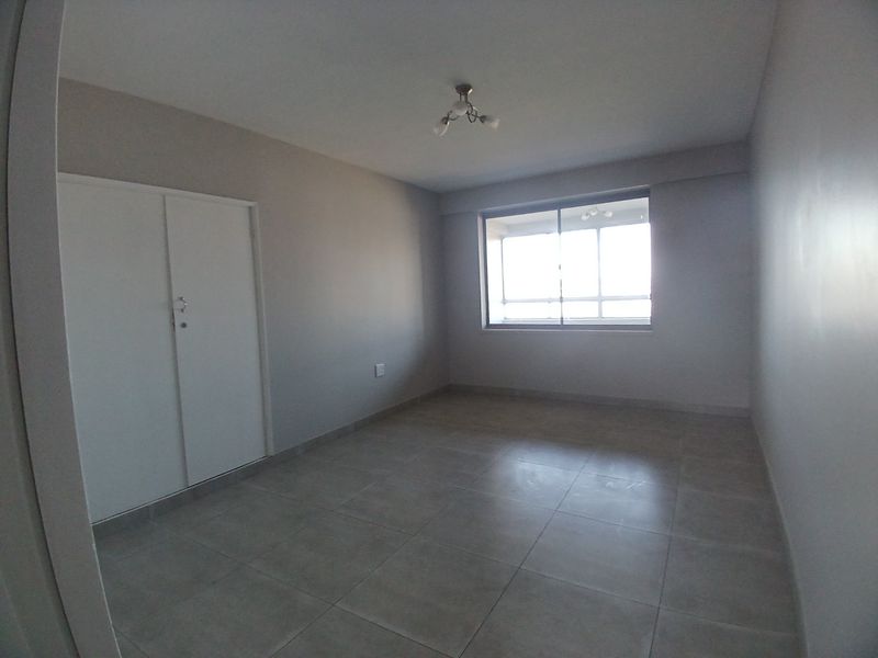 A vacant bedroom featuring neutral tiled flooring, a built-in wardrobe, and a large sliding window providing natural light.