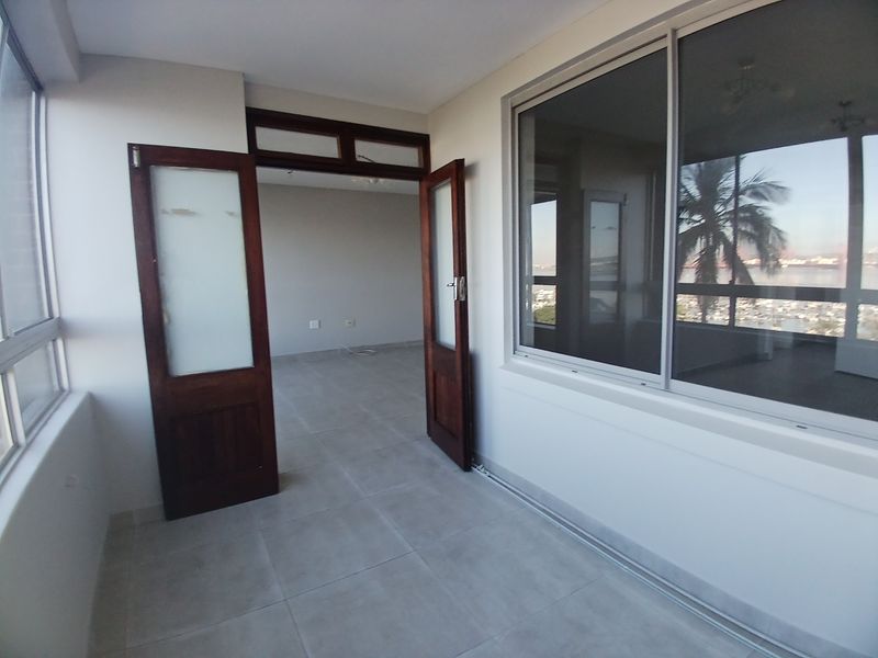 An enclosed balcony or sunroom featuring tiled flooring, large sliding windows, and timber-framed glass doors leading into the main living area.