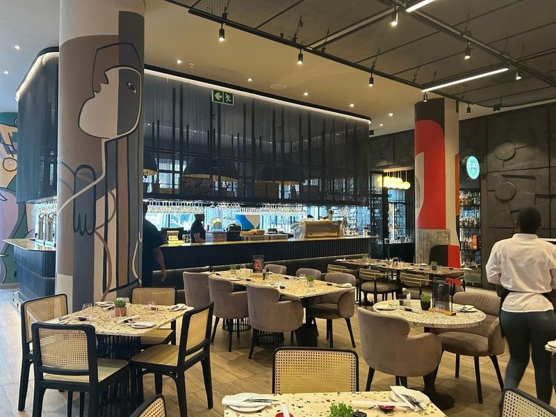 A modern, stylish bar area featuring a prominent service counter, artistic structural columns, and contemporary industrial-style ceiling lighting.