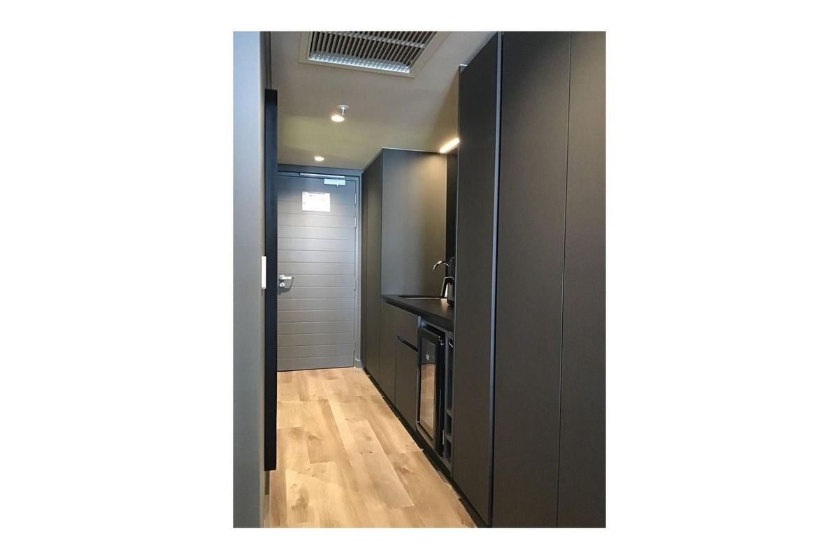 A compact, modern kitchenette featuring sleek dark cabinetry, integrated sink, and light wood-look flooring in a minimalist apartment setting.
