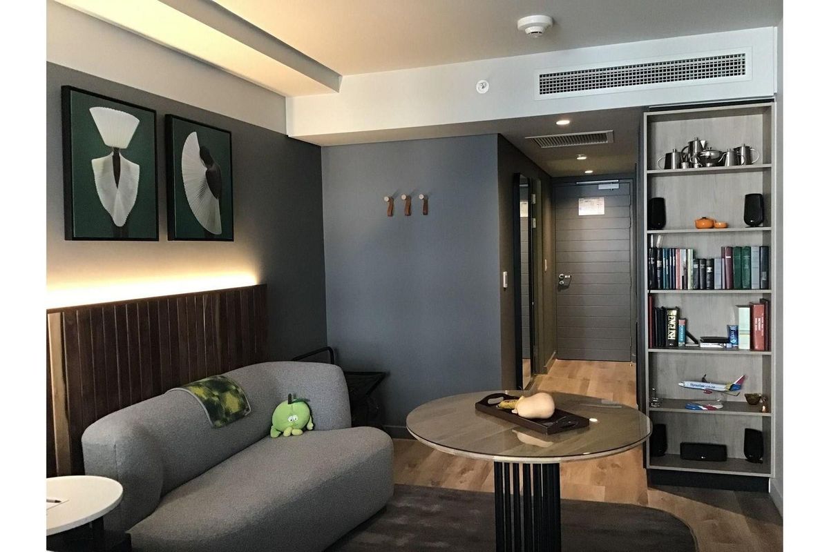 A modern living area featuring timber flooring, recessed ceiling lighting, ducted air conditioning, and a built-in shelving unit.