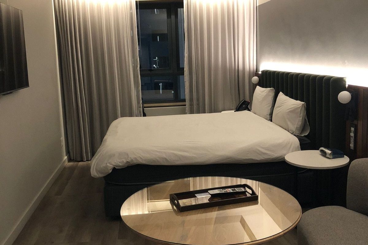 A modern, well-appointed bedroom featuring recessed ceiling lighting, high-quality laminate flooring, and a stylish integrated headboard with built-in bedside lighting.