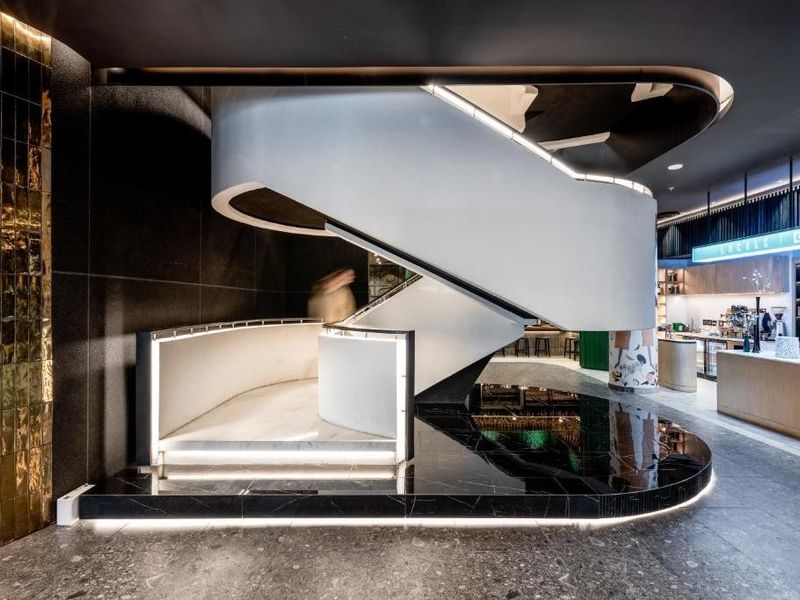 Modern open-plan interior featuring a striking curved staircase, premium marble flooring, and integrated architectural lighting in a sophisticated, high-end commercial or residential space.
