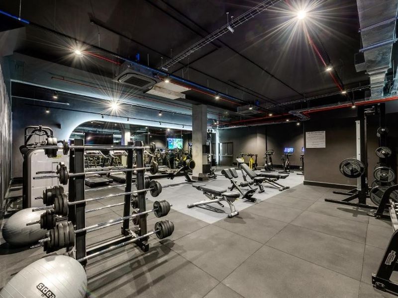 A modern, well-equipped fitness center featuring rubber flooring, exposed industrial-style ceilings, recessed lighting, and large mirrored walls for a professional workout environment.