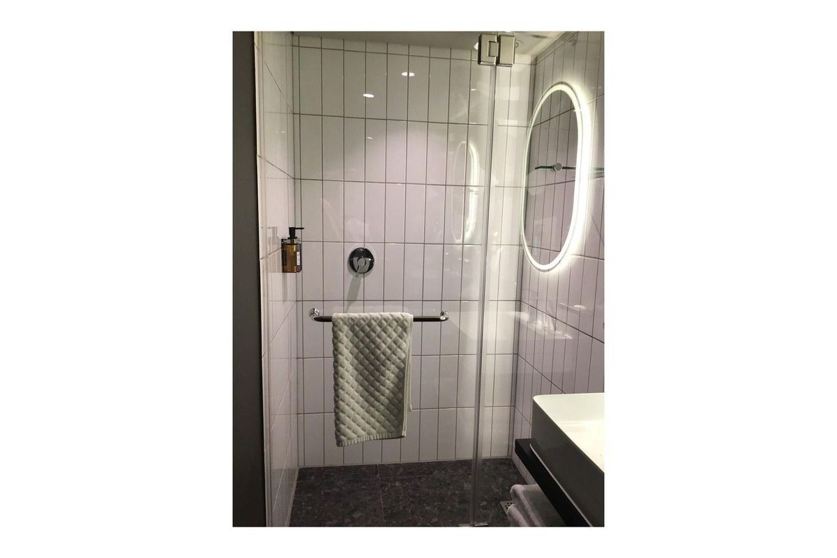Modern bathroom featuring a walk-in shower with glass screen, white subway-style wall tiles, dark floor tiles, and a contemporary backlit circular mirror.