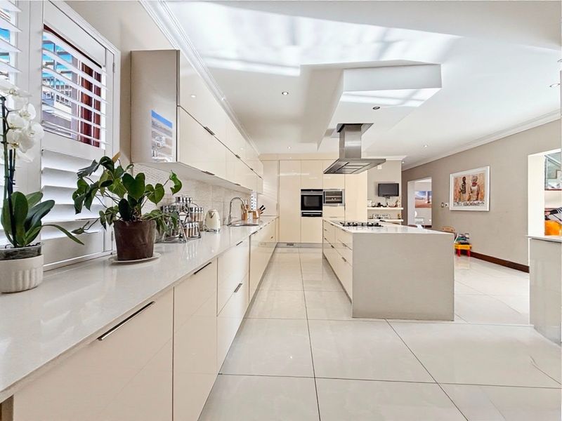 Modern, high-end kitchen featuring sleek high-gloss cabinetry, a large central island with a gas hob, integrated appliances, and polished floor tiles.