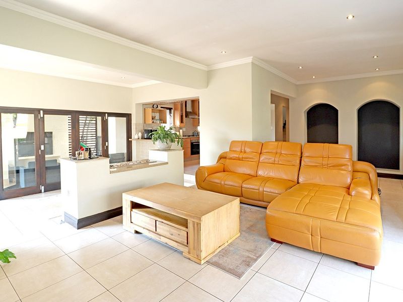 Spacious open-plan living area featuring neutral tiled flooring, recessed lighting, and architectural wall niches, seamlessly connecting to the kitchen and outdoor patio space.