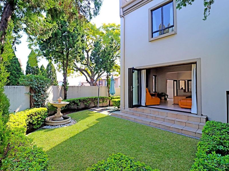 A well-maintained rear garden featuring a stone fountain, manicured lawn, and bi-fold doors providing seamless access to the interior living space.