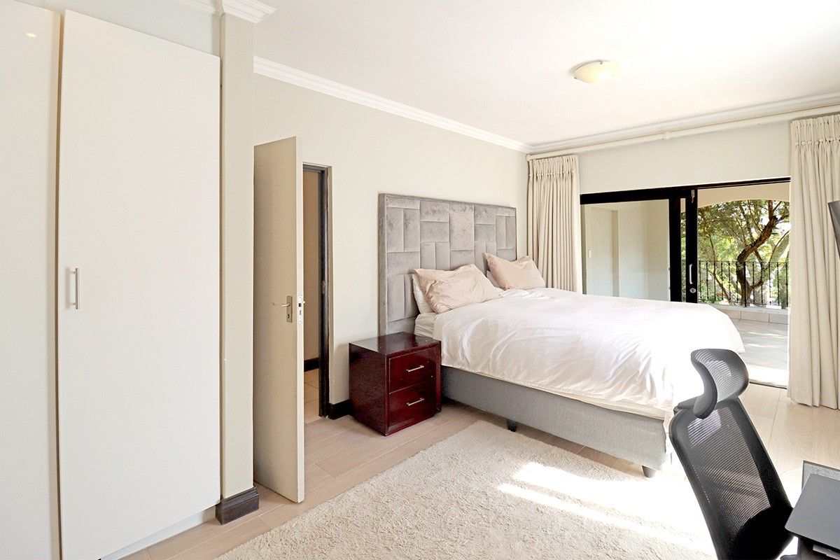 A bright bedroom featuring built-in cupboards, tiled flooring, and sliding glass doors that open onto a private balcony.