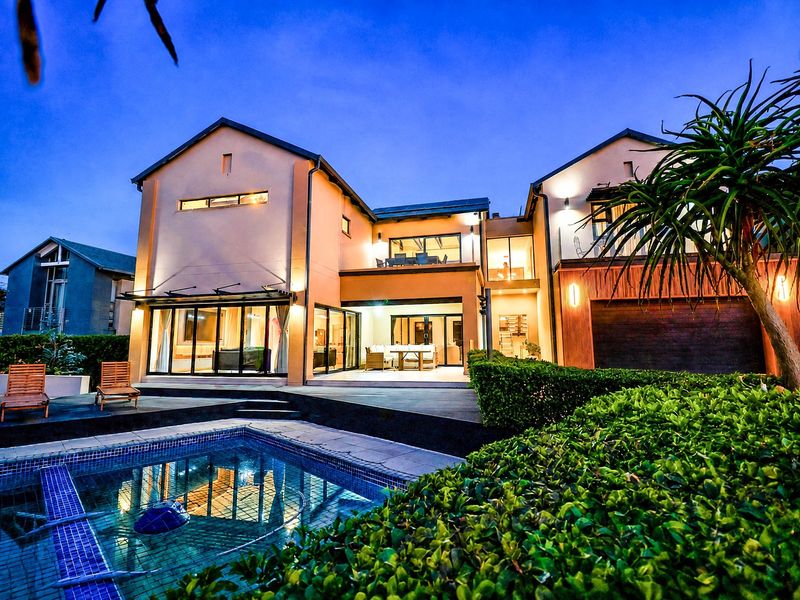 A beautifully illuminated rear elevation featuring a modern swimming pool, spacious patio, and upper-level balcony, showcasing contemporary architectural design and outdoor living space.