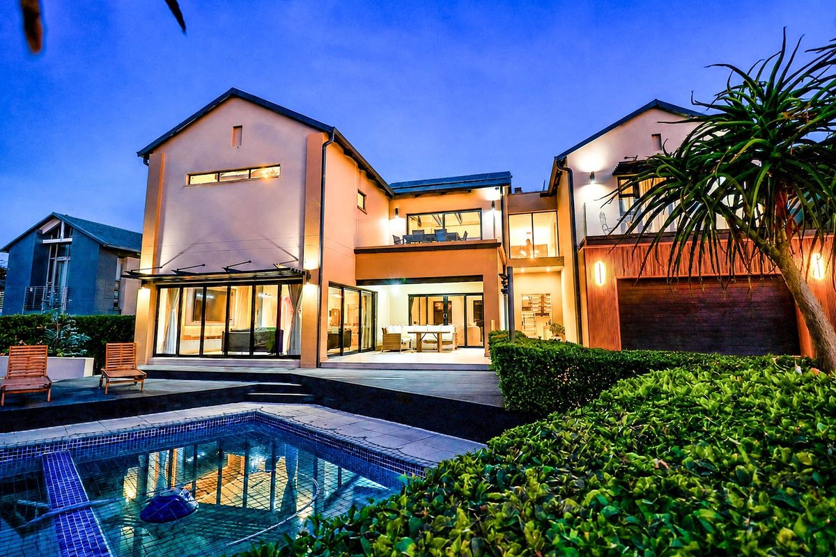 A beautifully illuminated rear elevation featuring a modern swimming pool, spacious patio, and upper-level balcony, showcasing contemporary architectural design and outdoor living space.