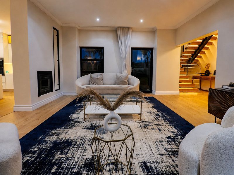 Spacious open-plan living area featuring timber flooring, a modern built-in fireplace, and an elegant timber staircase with glass balustrading.