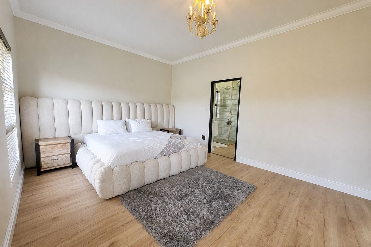 Spacious bedroom featuring light laminate flooring, crown molding, a decorative chandelier, and direct access to an en-suite bathroom.