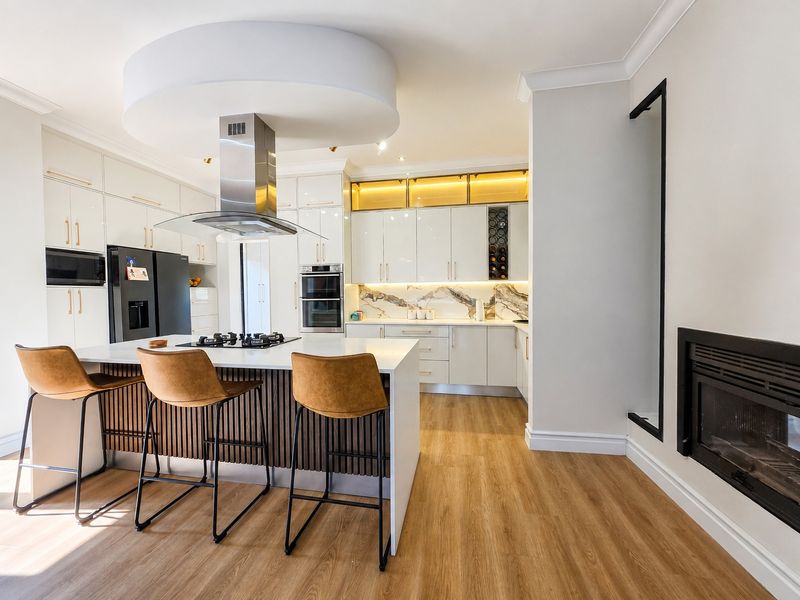 Modern kitchen featuring a central island with gas cooktop, high-gloss cabinetry, integrated appliances, stone splashback, and an adjacent fireplace.