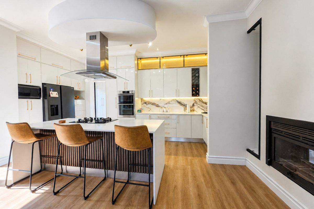 Modern kitchen featuring a central island with gas cooktop, high-gloss cabinetry, integrated appliances, stone splashback, and an adjacent fireplace.