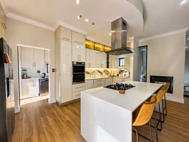 Modern kitchen featuring a central island with gas hob, built-in oven, stone countertops, and an adjacent scullery area with high-end cabinetry.