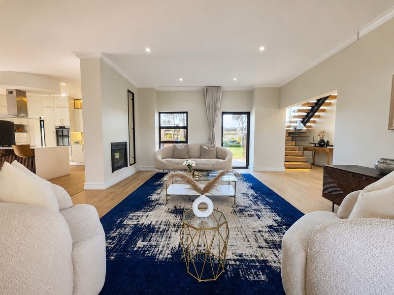 Spacious open-plan living area featuring a modern kitchen, built-in fireplace, and a striking timber staircase with glass balustrade, leading to a bright garden view.