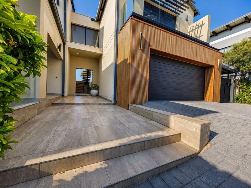 Modern front facade featuring a double garage with timber slat cladding, paved driveway, and tiled entrance steps leading to the main doorway.