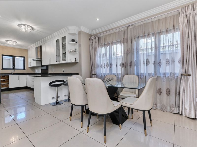 An open-plan kitchen and dining area featuring white cabinetry, granite countertops, tiled flooring, and elegant crown molding with recessed and flush mount lighting.