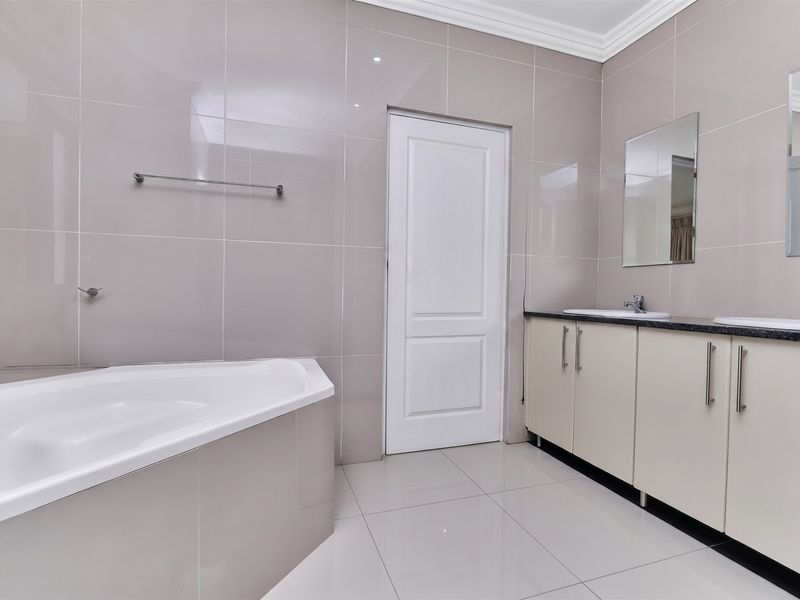 A clean, modern bathroom featuring a corner bathtub, double vanity with built-in cabinetry, and neutral wall-to-floor tiling.