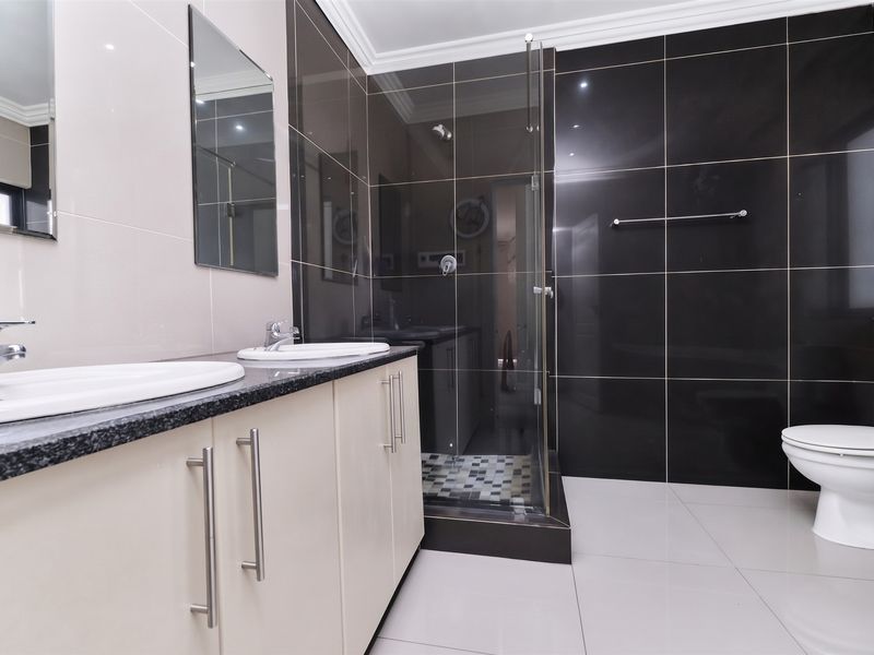 Modern bathroom featuring a double vanity with granite countertop, a glass-enclosed shower with dark feature tiling, and a clean, contemporary aesthetic.