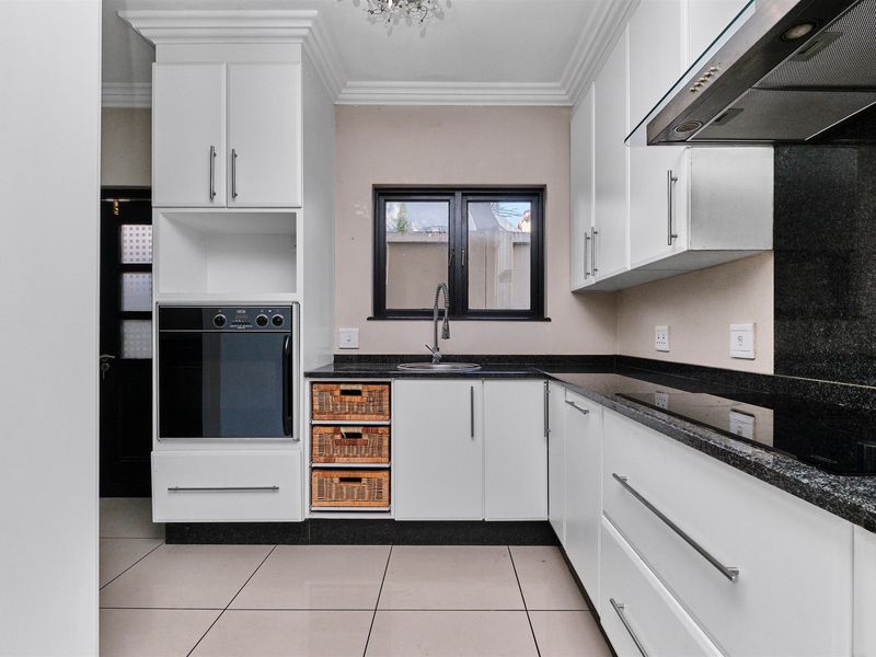 Modern kitchen featuring white cabinetry, granite countertops, built-in oven, extractor fan, and tiled flooring with a clean, contemporary finish.
