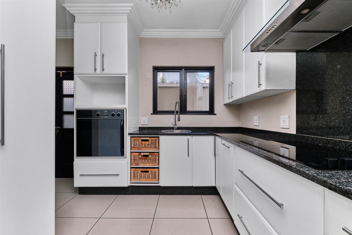 Modern kitchen featuring white cabinetry, granite countertops, built-in oven, extractor fan, and tiled flooring with a clean, contemporary finish.