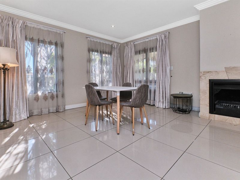 A bright dining room featuring large windows, tiled flooring, and a built-in fireplace with stone surround.