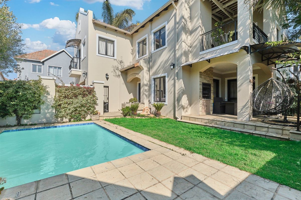 Rear exterior view featuring a swimming pool, a covered patio with a built-in braai, and an upper-level balcony.